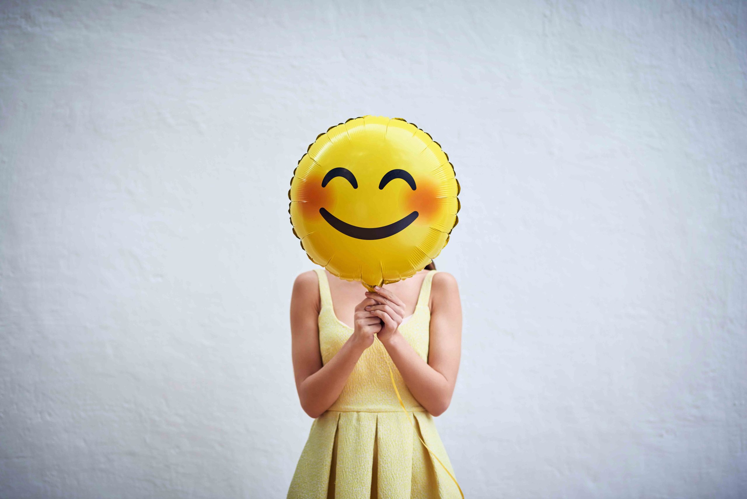 woman holding a smiling emoji balloon hiding her face